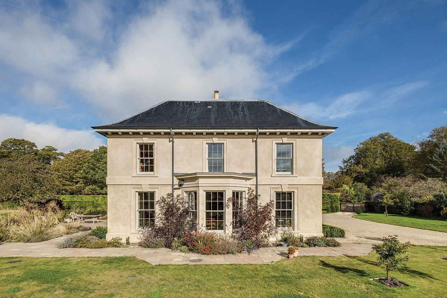 A large, elegant country house with a slate roof and lime render and Bath stone facade.  Large classical bay window 