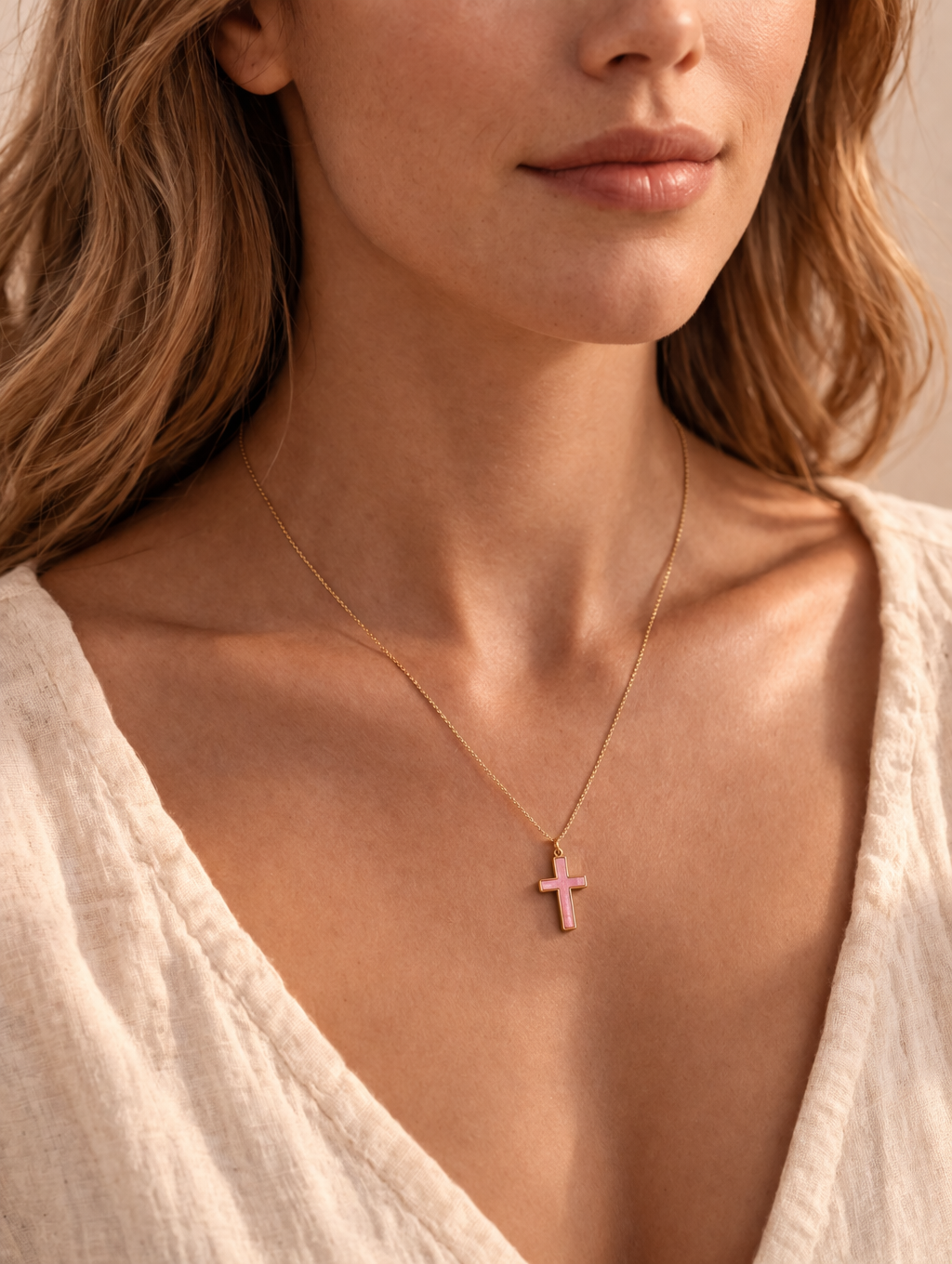Close-up of a woman wearing a light beige top and a gold necklace with a pink cross pendant.
