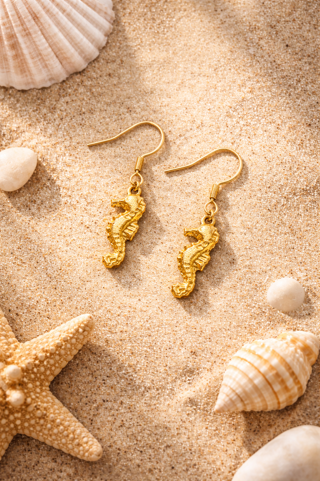 Golden seahorse earrings on sandy beach