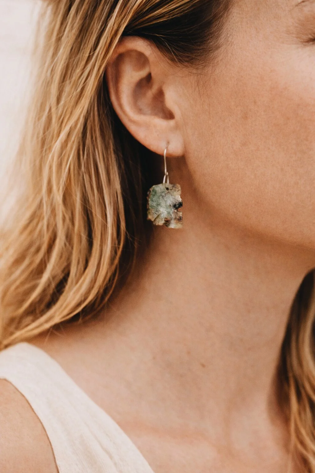 Close-up of a woman's ear wearing a dangling earring made of a rough, textured stone or mineral.