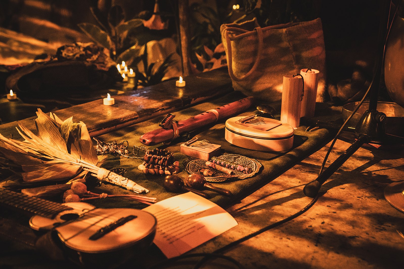 A collection of small items and jewelry displayed on a cloth-covered surface, illuminated by candlelight, with plants and candles in the background.