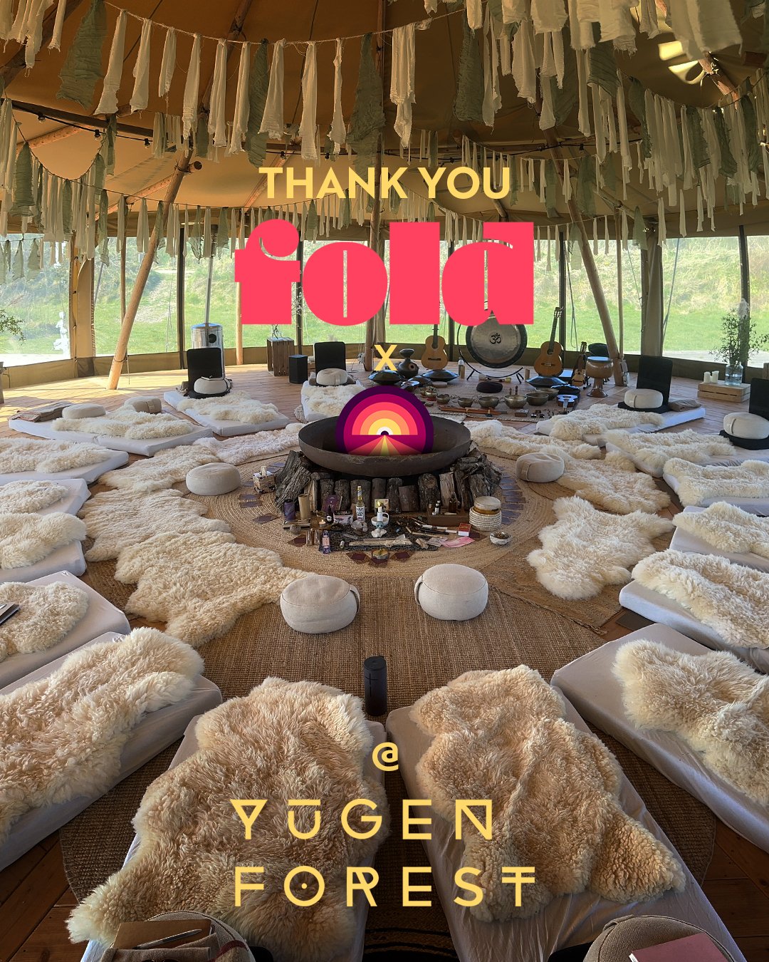 Interior of a tipi-style structure decorated with hanging fabric strips and outdoor views visible through large windows. The space features a central fire pit surrounded by white cushions and fur throws, arranged in a circle for seating. The setup includes musical instruments and decorative items. The overlay text reads 'Thank You Solo @Yugen Forest'.