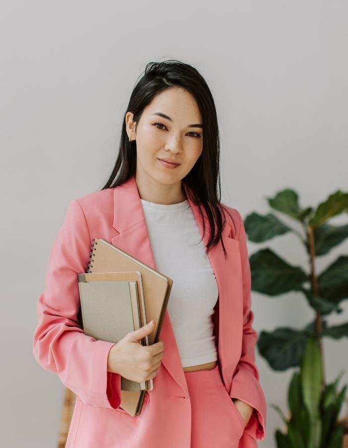 Women in pink business suit smiling at the camera holding a notebook.