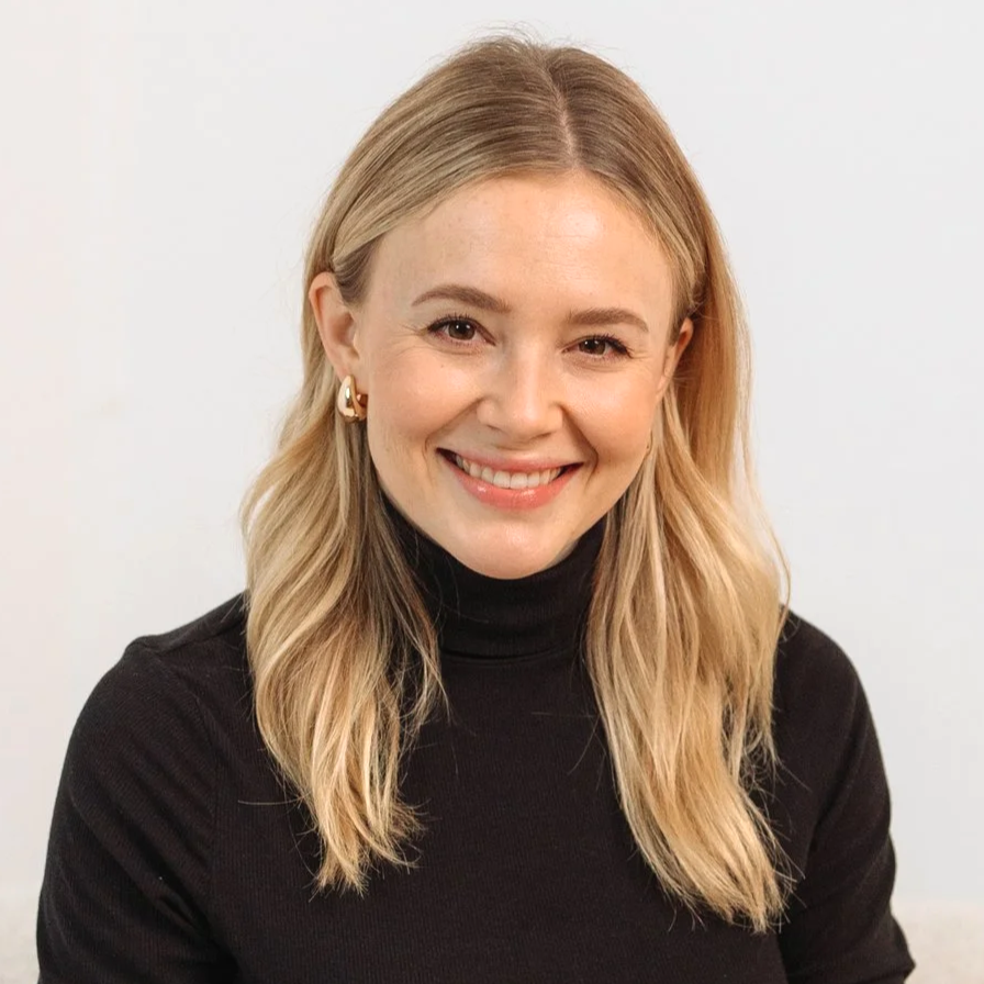 Larissa Weiss. Lächelnde junge Frau mit blonden, mittellangen Haaren, tragend schwarze Rollkragenpullover und goldene Ohrringe, vor hellem Hintergrund.