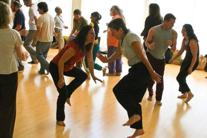 People dancing and socializing in a bright room with wooden floors.