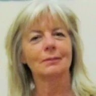 A woman with blonde hair, wearing a light-colored top, looking at the camera with a slight smile.