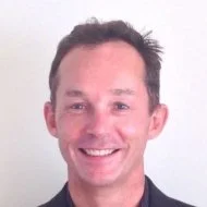 A smiling man with dark hair and a fair complexion against a plain light background. Andrew webb, biodanza facilitator in Warwickshire, Leamington Spa.