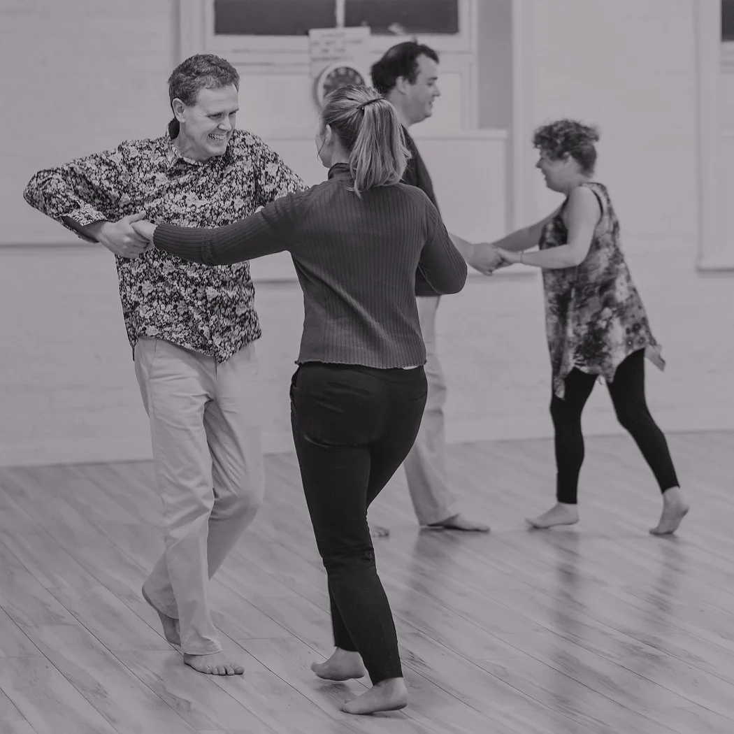 Four people dancing in a room, holding hands, smiling, and enjoying themselves.