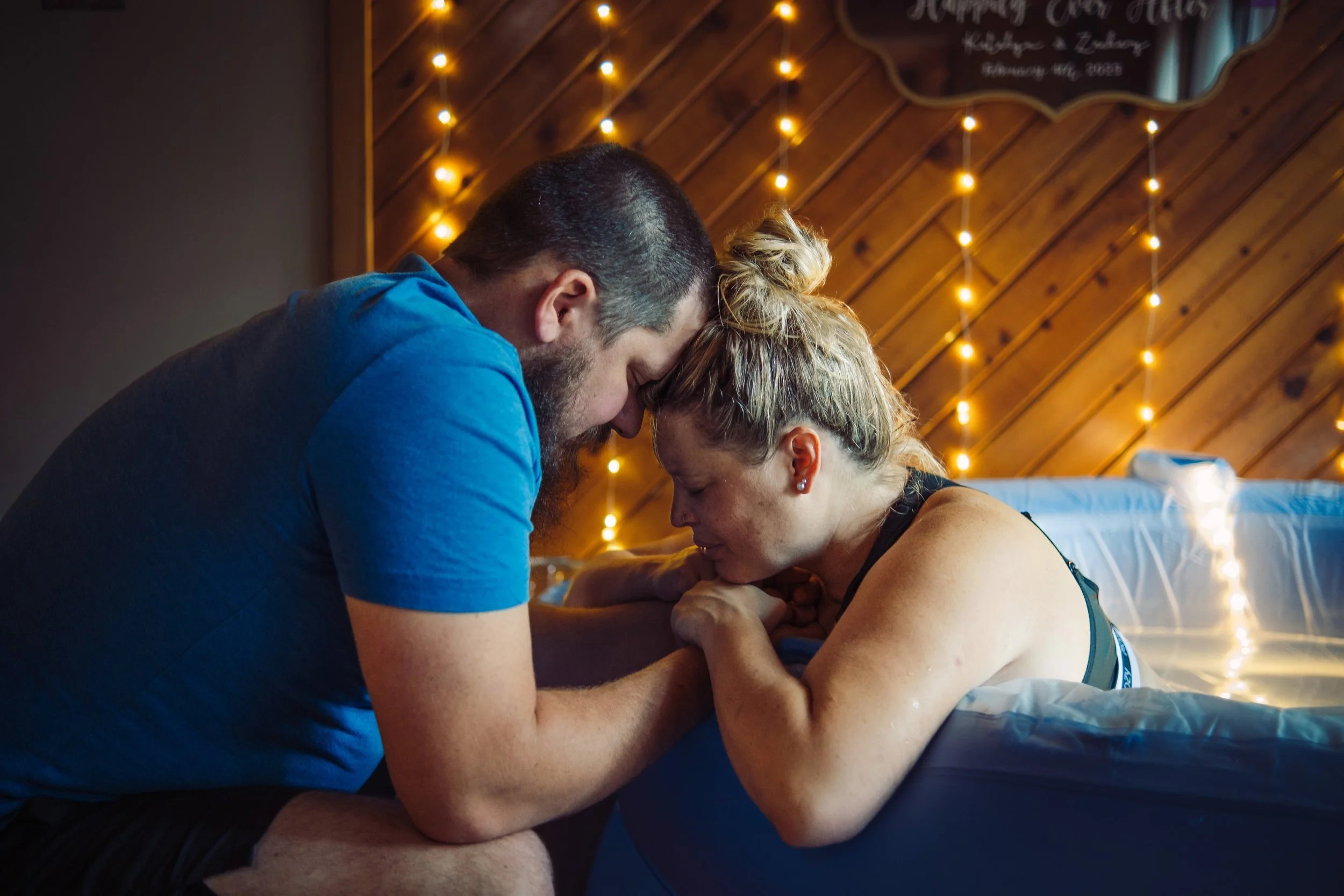 Laboring mother holding hands with her partner for support in a home birth pool in Traverse City Michigan.