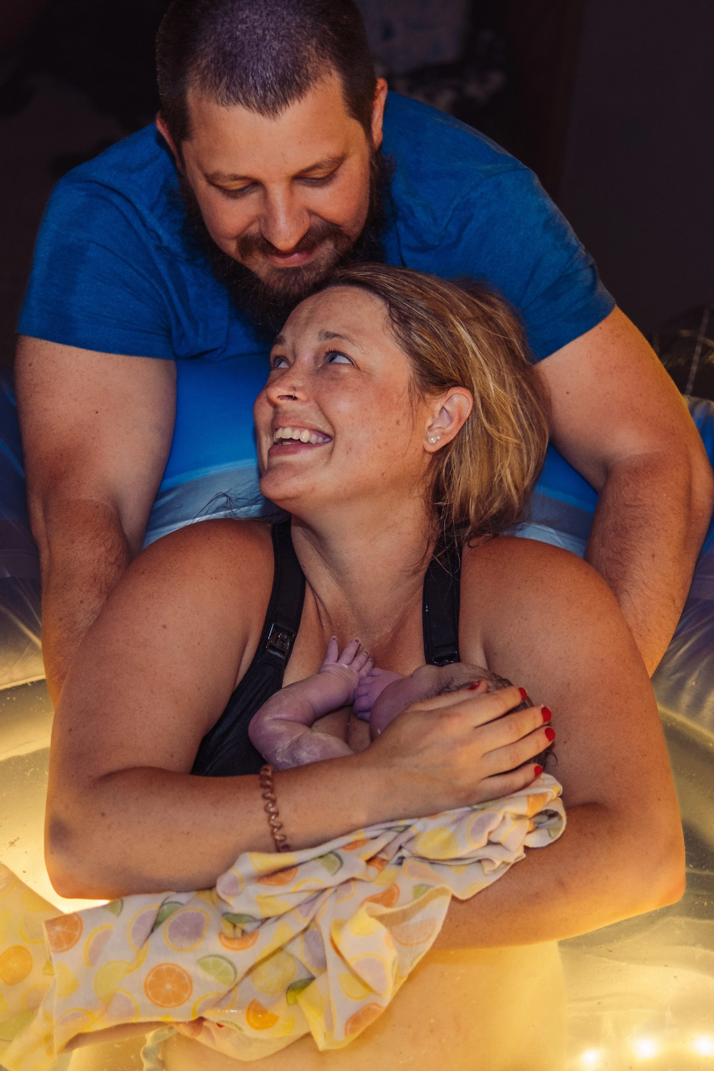 Parents smiling with their newborn baby immediately following a home water birth in Traverse City MI.