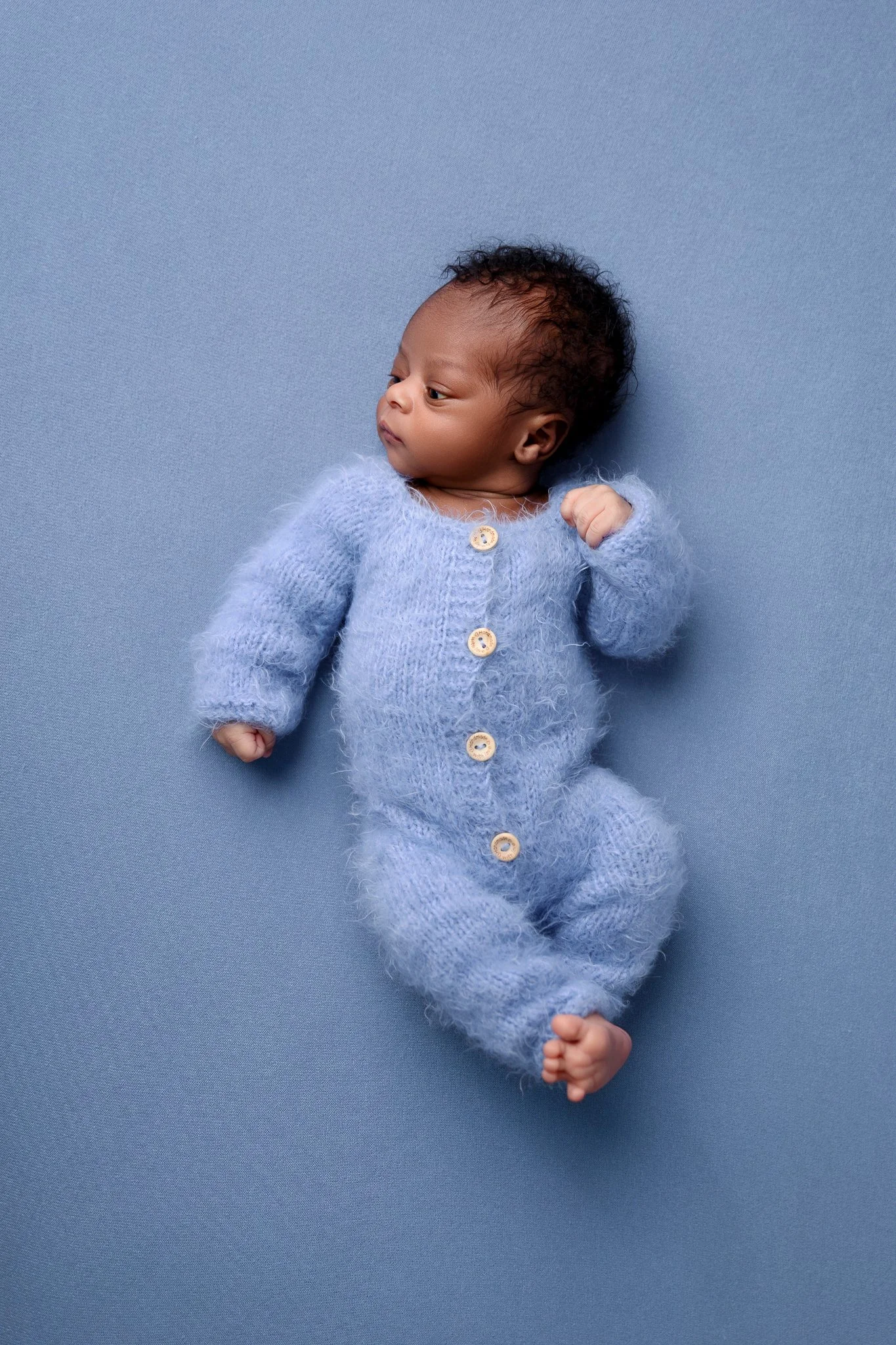 Newborn in blue onesie on blue backdrop.