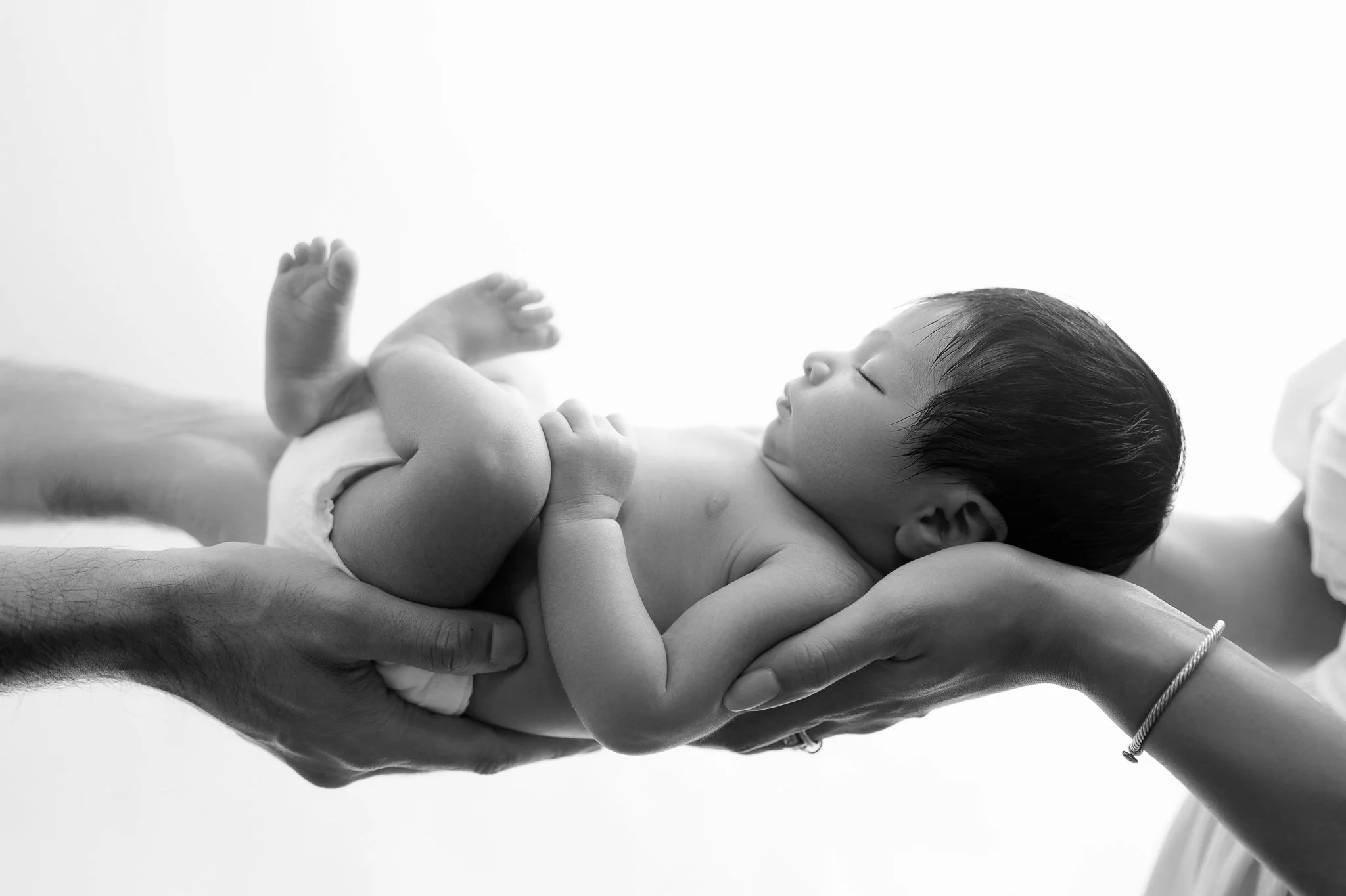 Two sets of hands are holding newborn baby.
