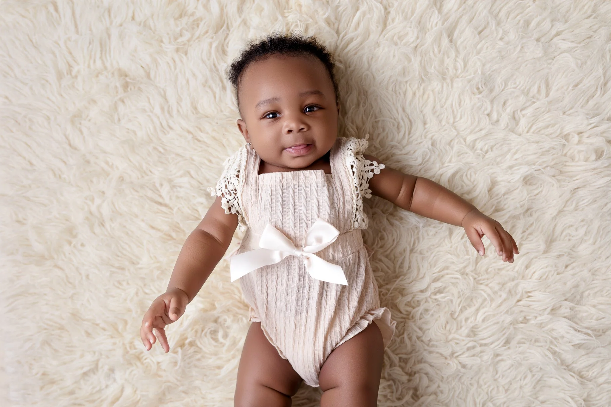A toddler is laying on her back, looking up at the camera.