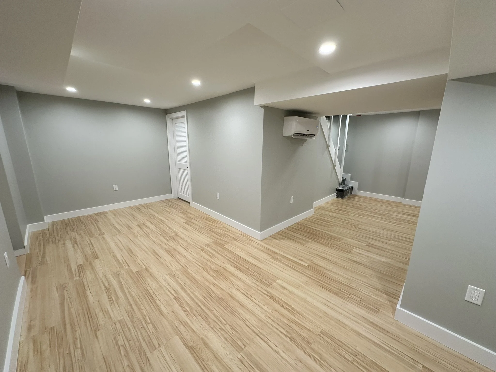 Finished basement with gray walls, wood-look flooring, recessed lighting and a wall-mounted mini-split.