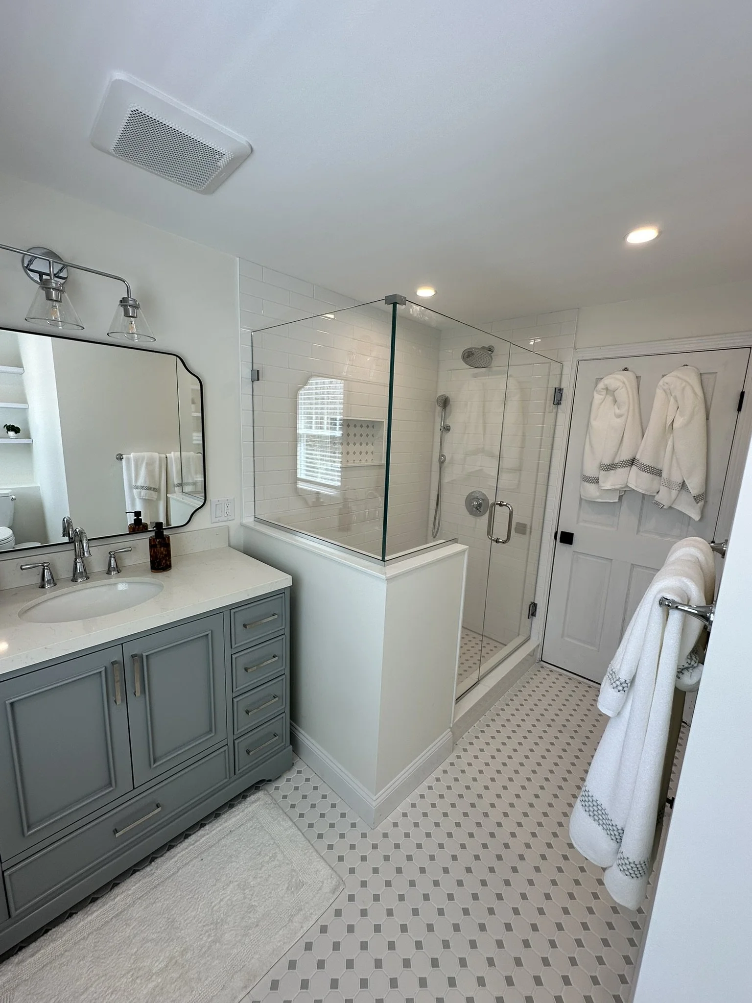 After: remodeled master bathroom with blue-gray vanity, glass shower enclosure, white tile and patterned tile floor.