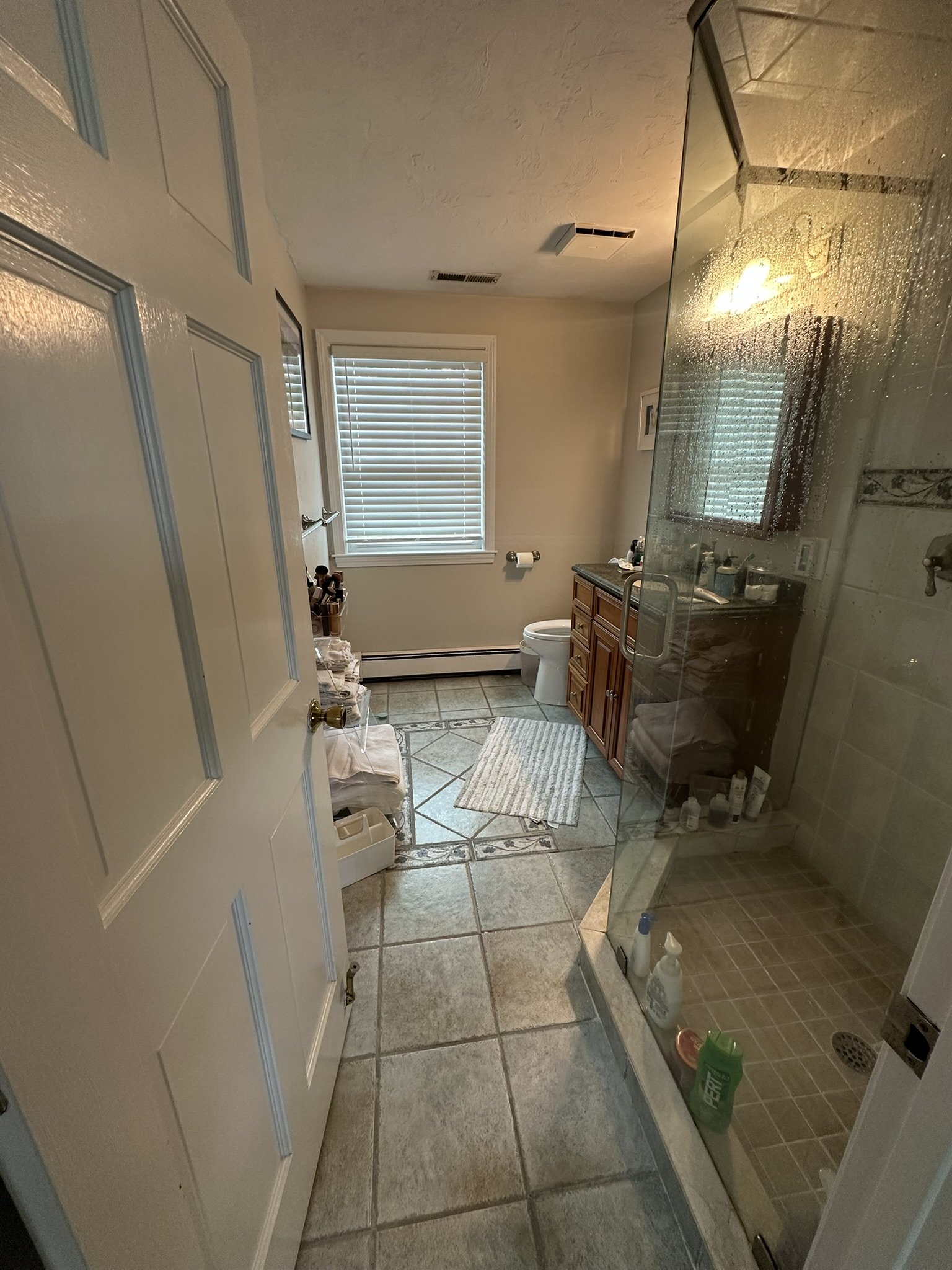 Before: master bathroom with wood vanity, tiled shower enclosure and existing tile floor.