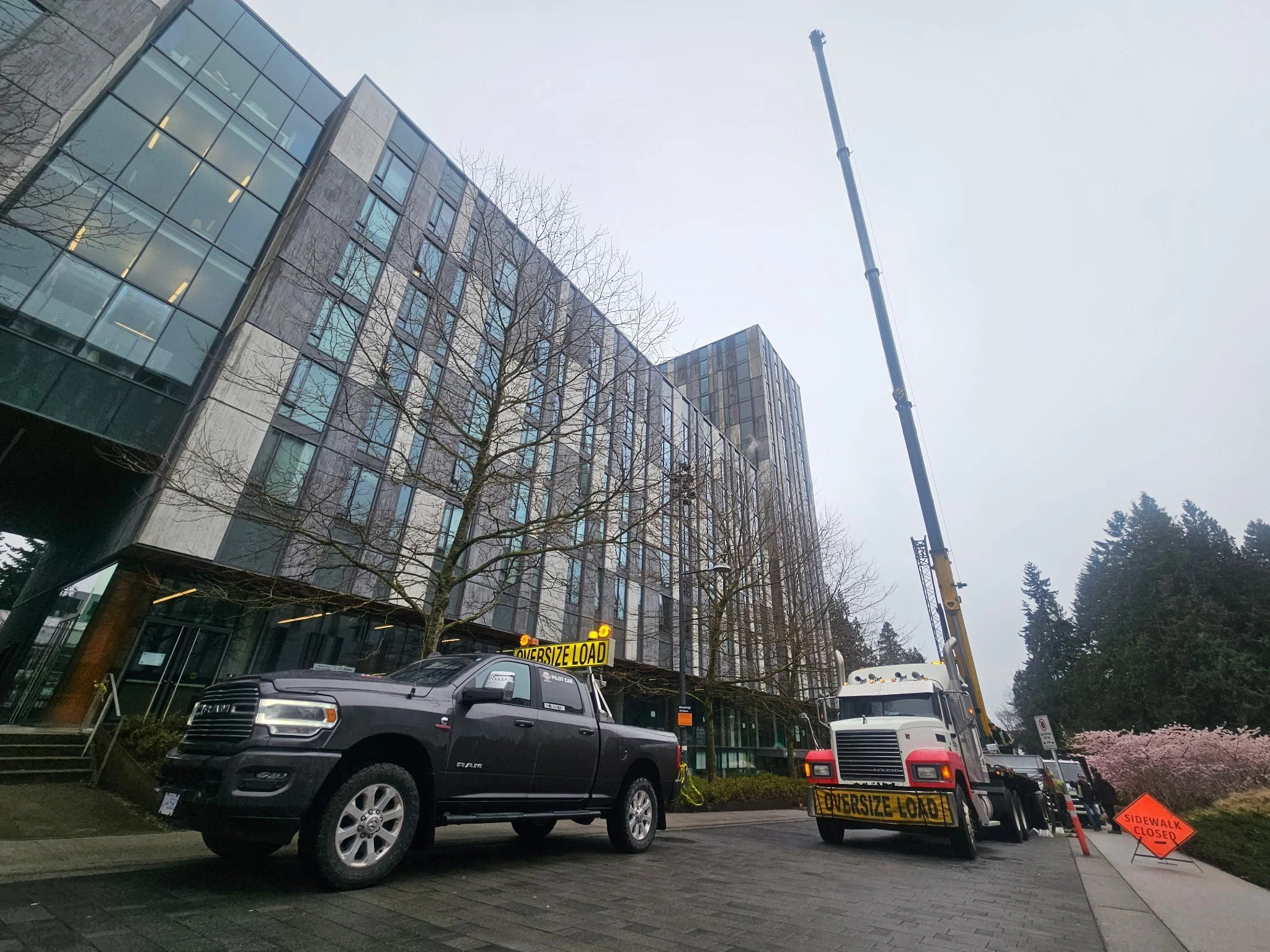 Construction crew working on building exterior with crane, truck, and traffic signs indicating sidewalk is closed.