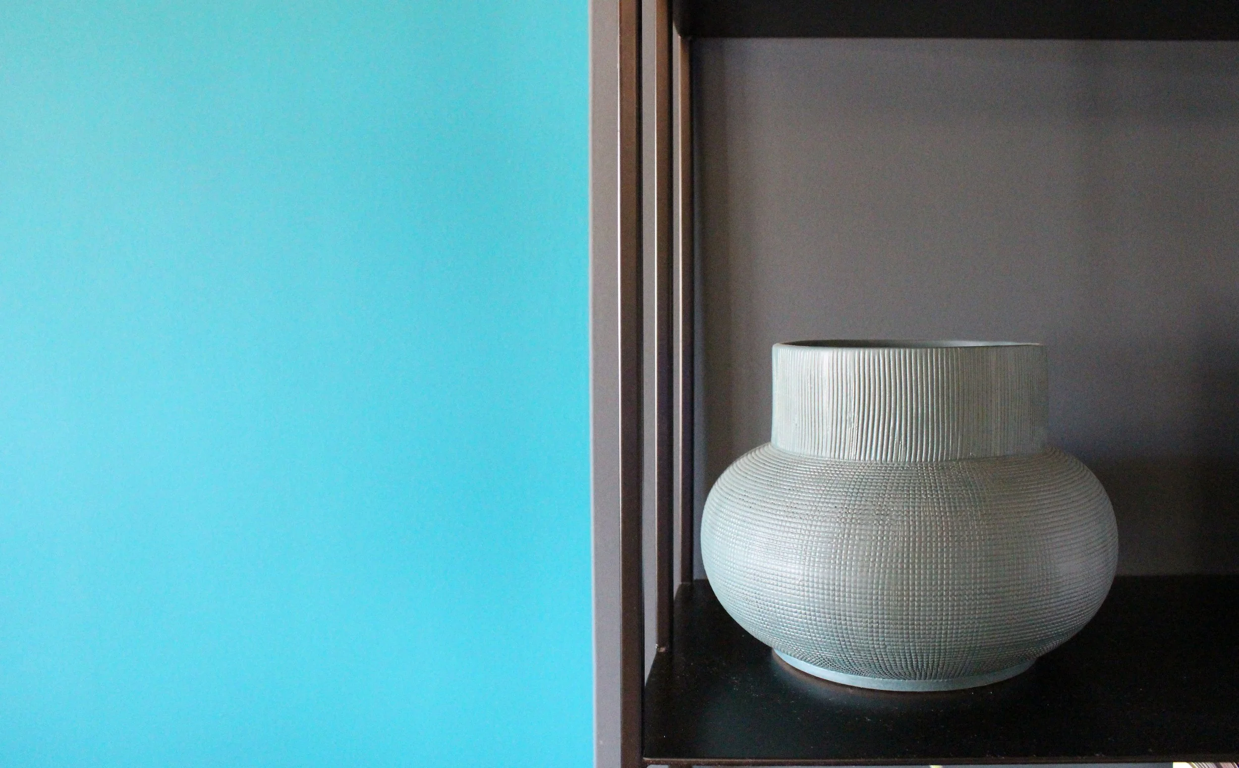 A ceramic vase with a textured, ribbed pattern sitting on a black shelf.