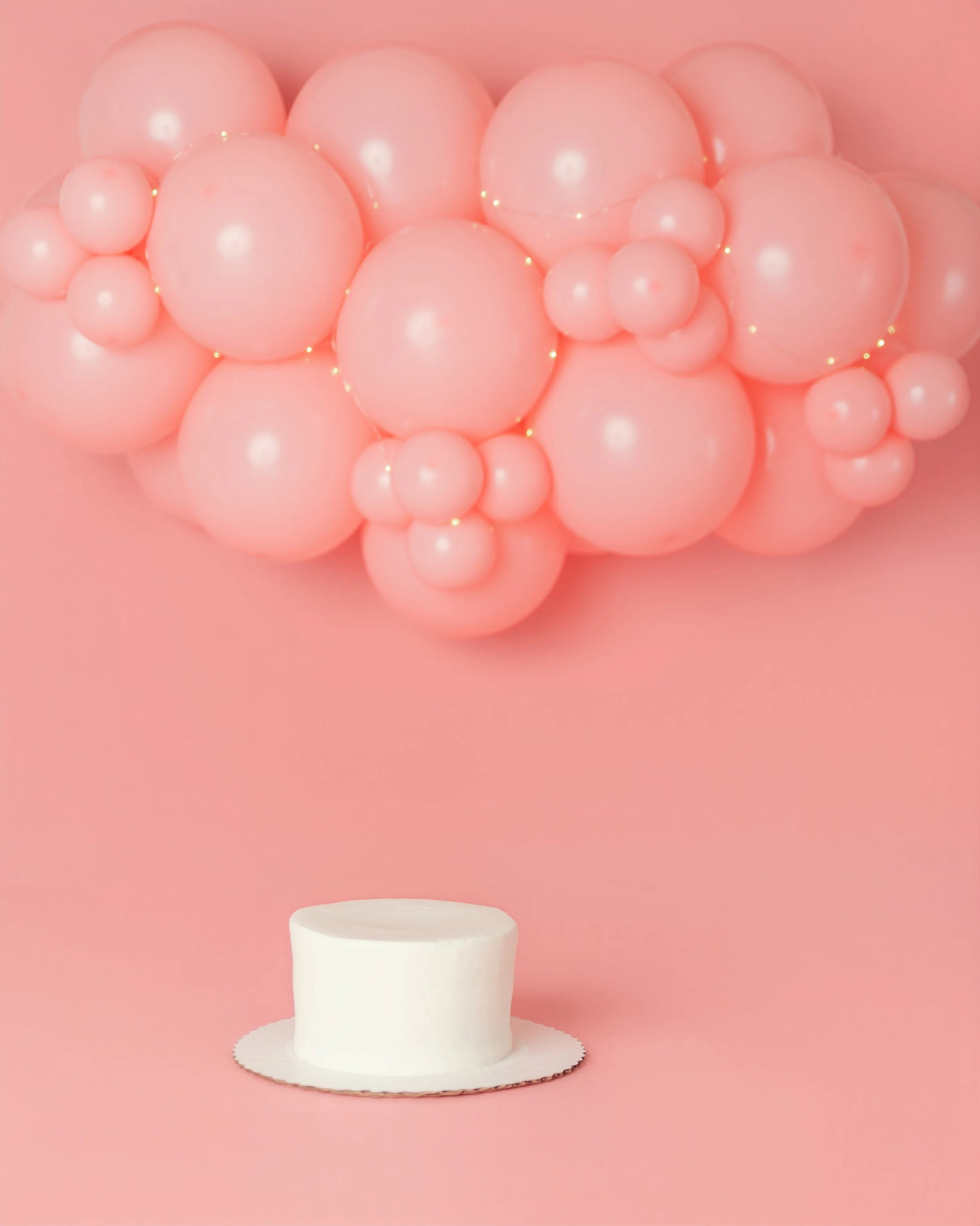 A monochrome cake smash set in bubblegum pink with balloons and twinkle lights.