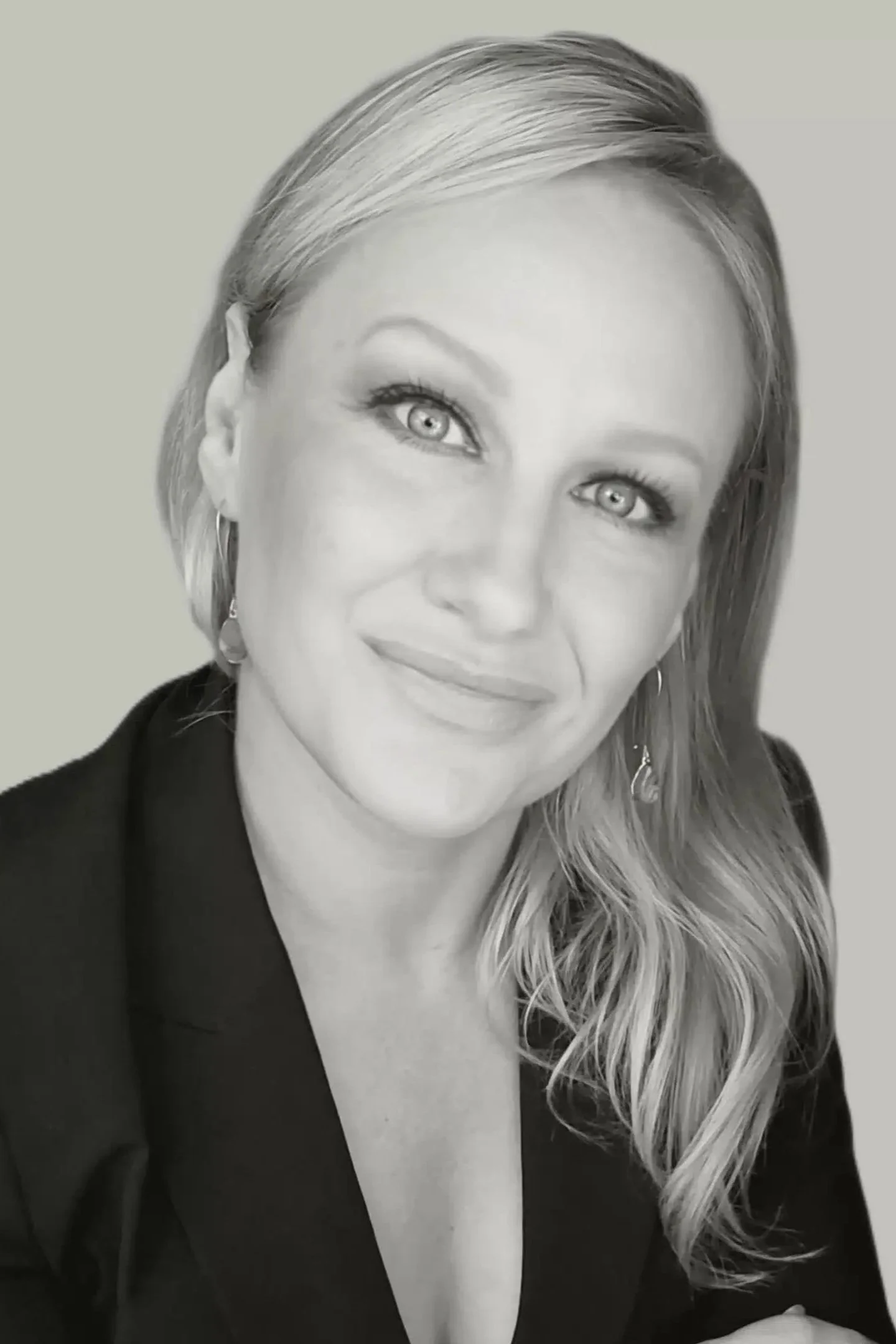 Black-and-white portrait of a smiling woman with shoulder-length wavy hair, wearing earrings and a blazer.