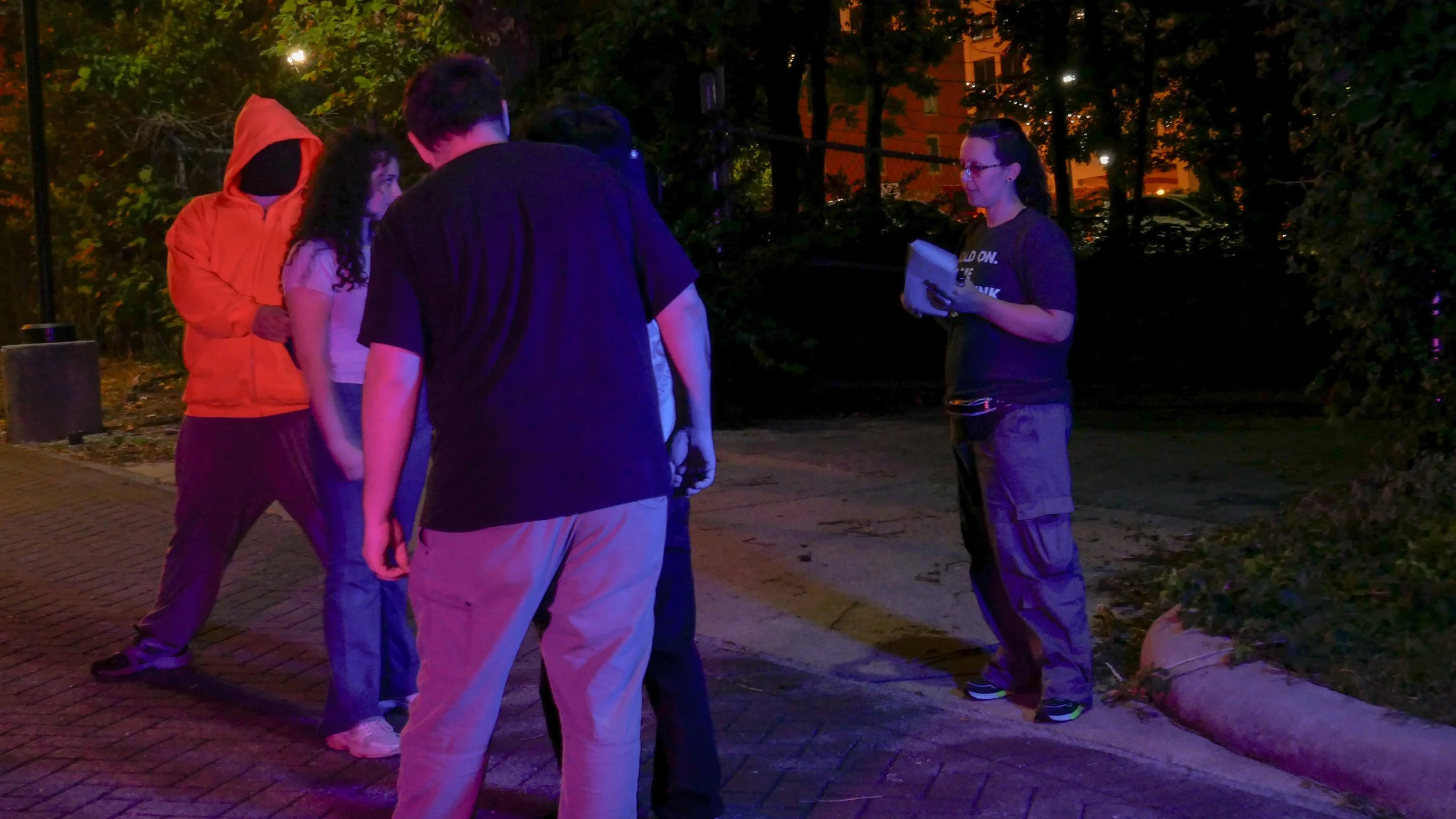 Director Alyssa Malloy stands near two actors on a dimly lit city sidewalk, overseeing a nighttime mugging scene for the short film In Reverie.