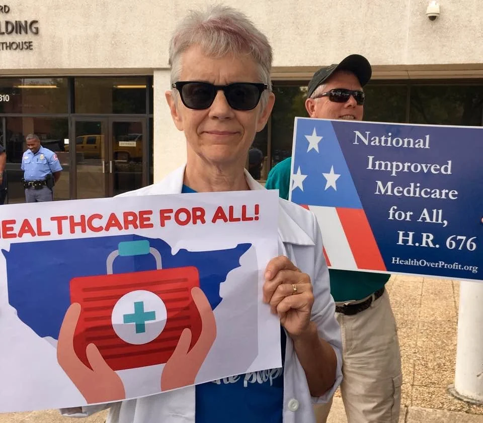 Photo of Patti Reiser holding a sign that says "Healthcare for All!"