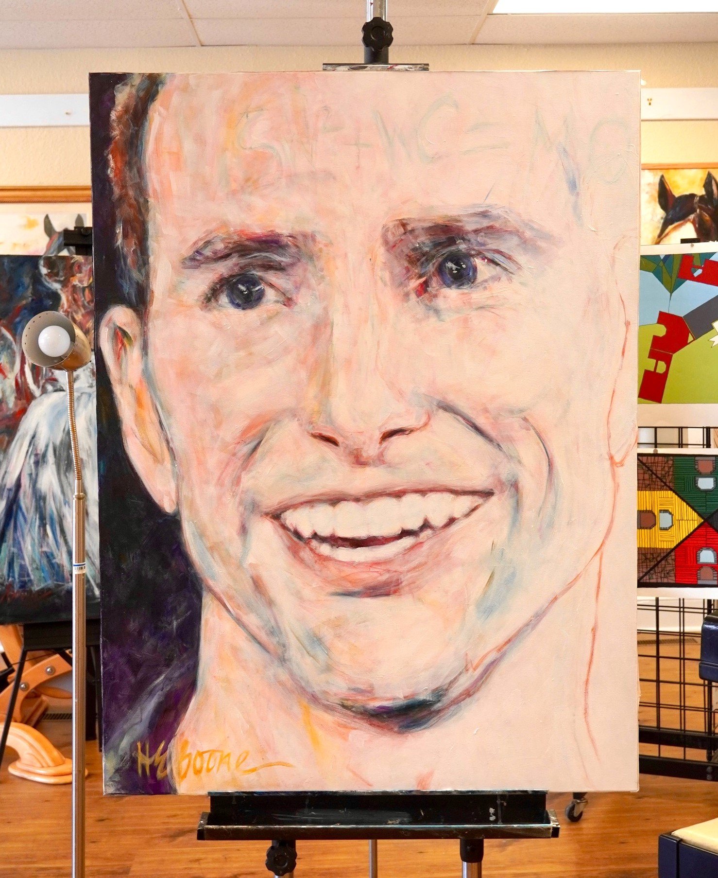 A large, colorful portrait painting of a smiling man with dark eyes and brown hair, and a signature signed at the bottom left.