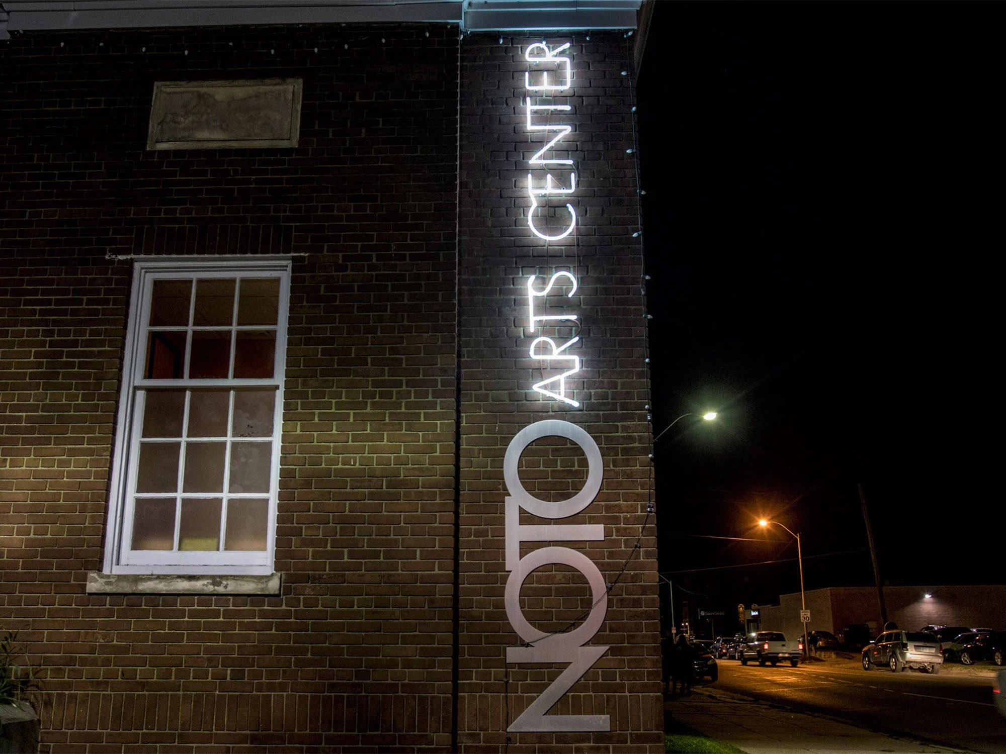 Night view of a brick building with a large vertical neon sign that reads 'ZODIAC ARTS CENTER' on the side.