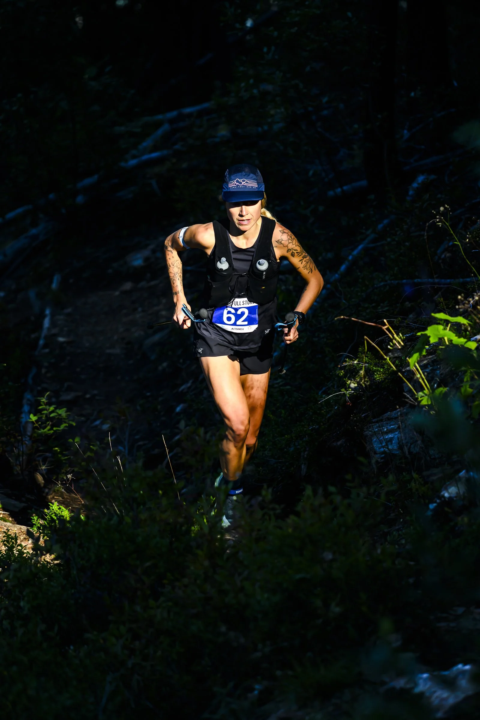 Female trail runner with bib number 62 running through a dark forested trail.
