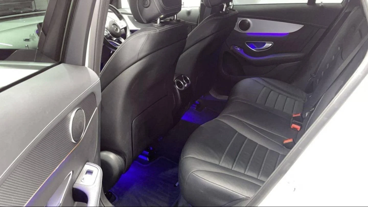 The interior of a modern luxury car with black leather seats, illuminated blue ambient lighting, and advanced control panels on the door.
