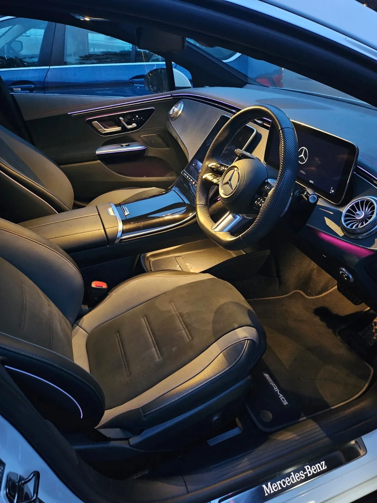 Interior of a Mercedes-Benz luxury car, featuring a digital dashboard, leather seats, a steering wheel with the Mercedes logo, and ambient lighting.