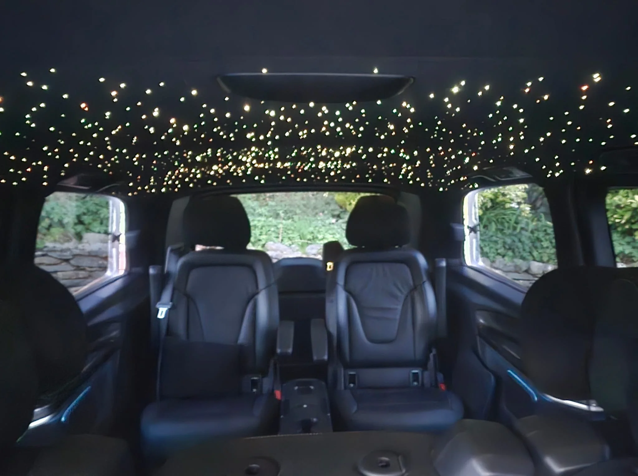 Interior of a Mercedes-Benz EQV showing a ceiling decorated with numerous small, glowing, star-shaped lights.
