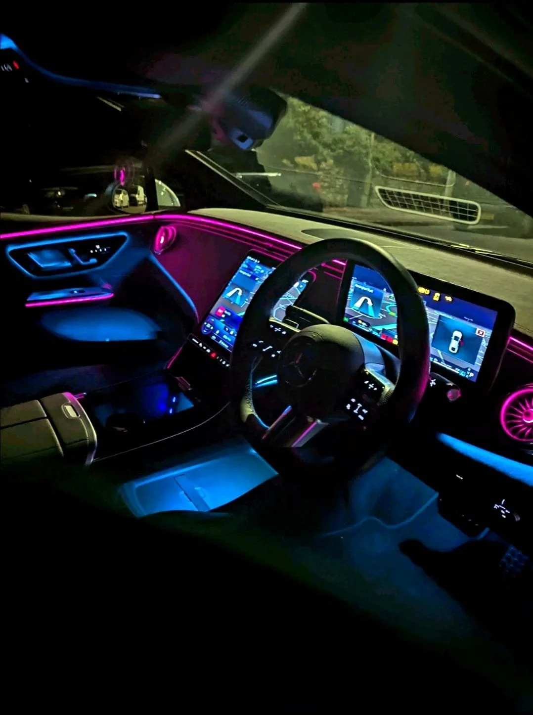 Interior of a modern car at night with neon pink and blue lighting, digital dashboards, and a steering wheel.