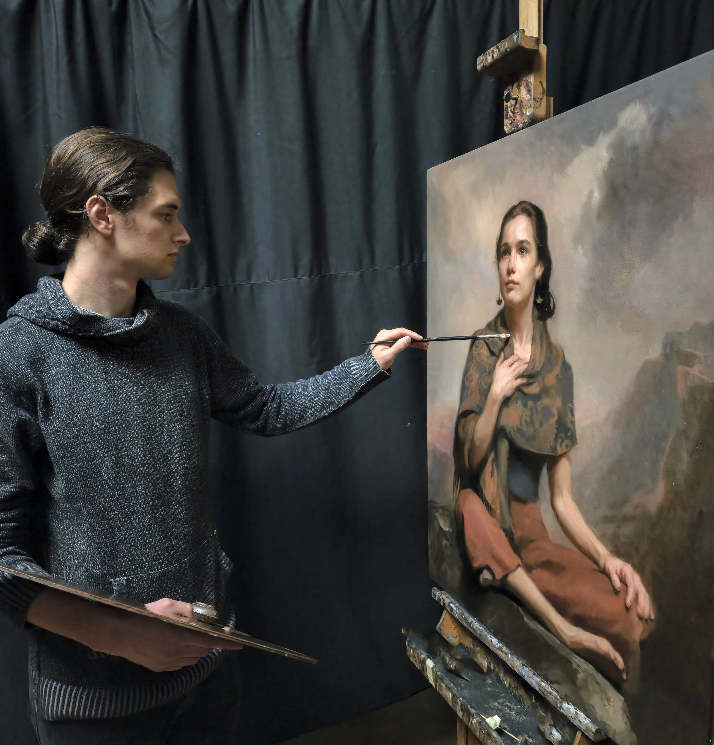 An artist with long dark hair, wearing a black sweater, is painting a realistic portrait of a woman on a large canvas. The artist is holding a paintbrush and is focused on his work. The background features dark curtains.