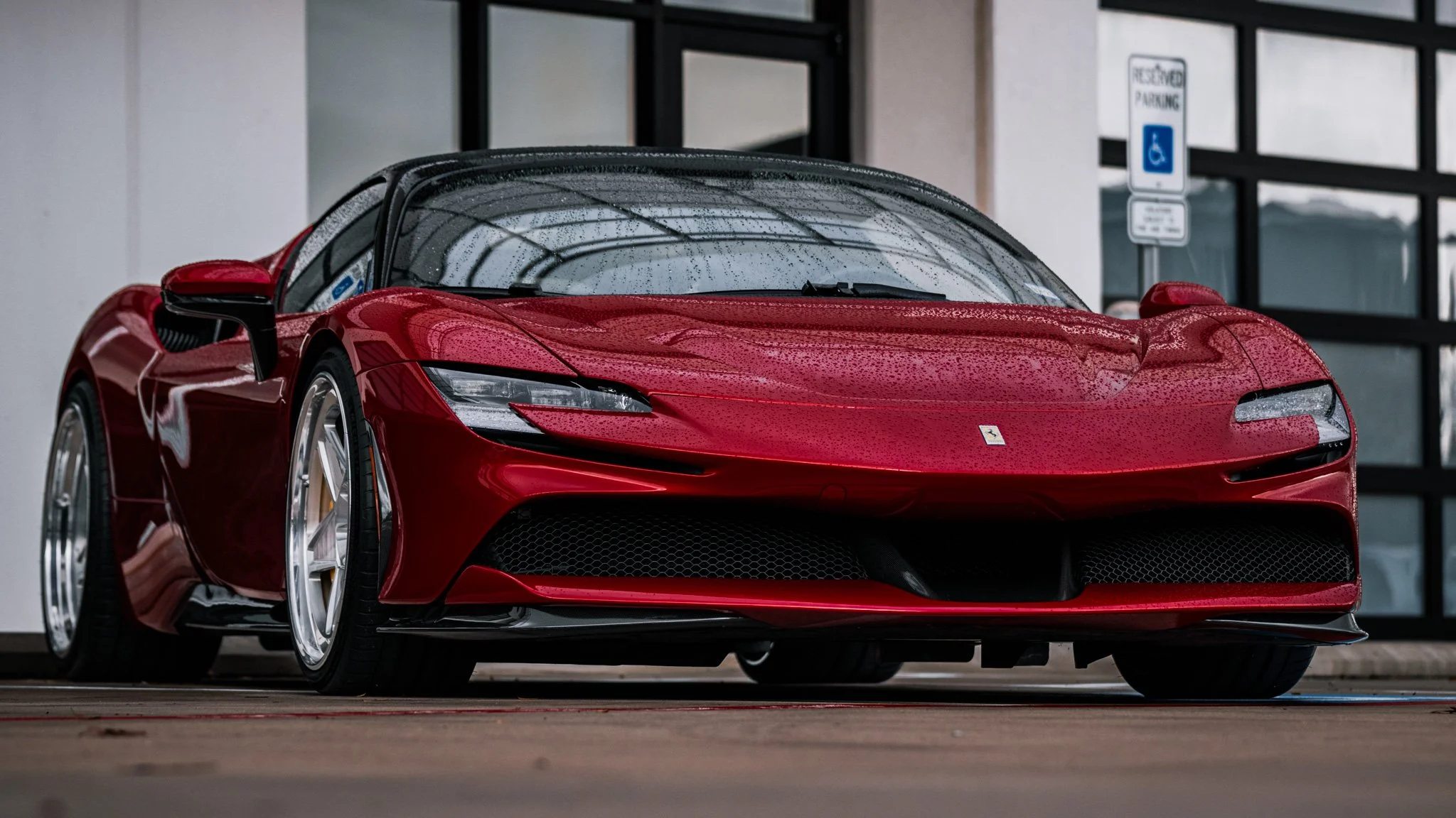 Red Ferrari sports car parked outside with rain droplets on the windshield and body