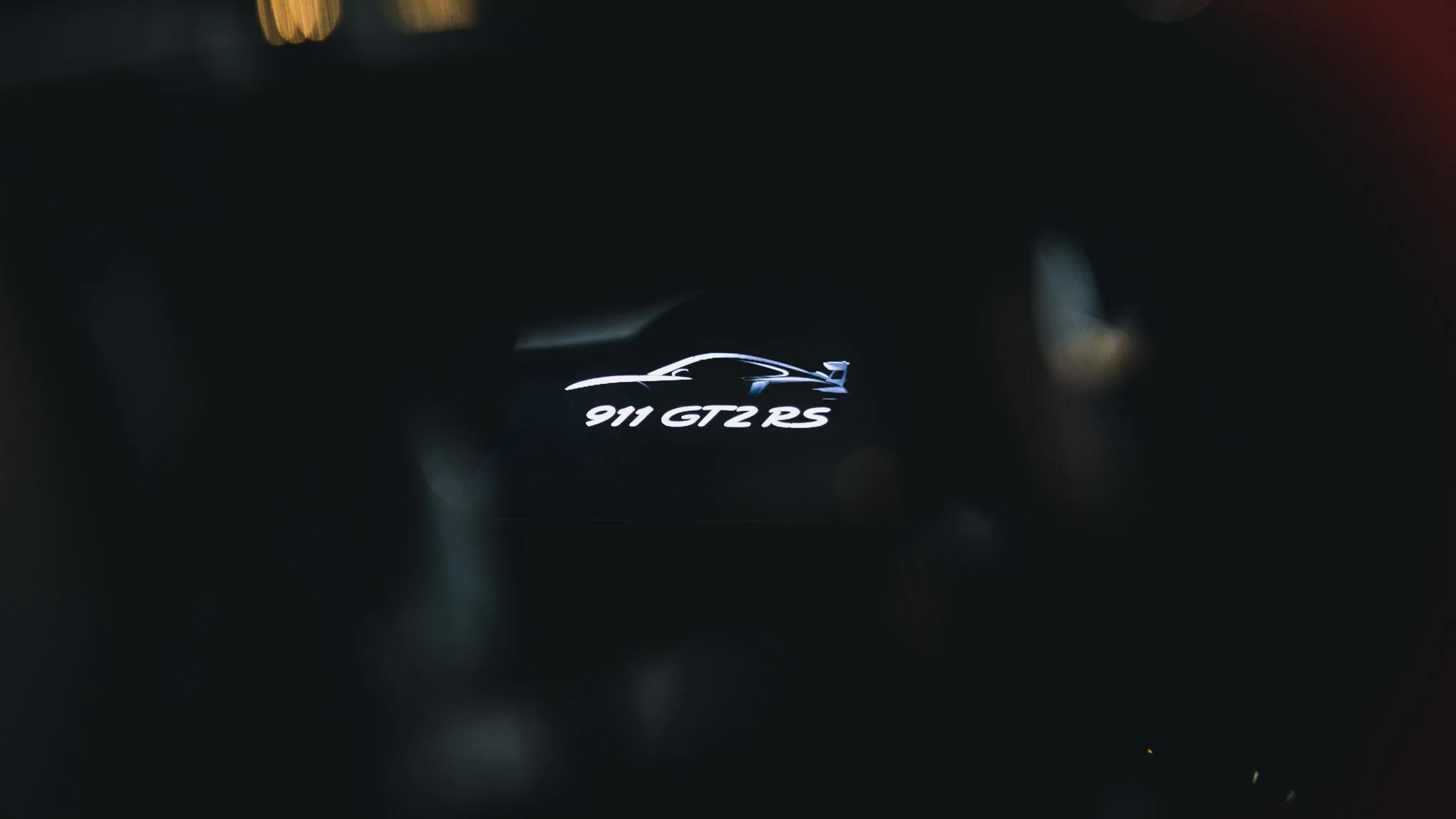 Close-up of a digital display showing the silhouette of a car and the text '911 GT2 RS' in a dark environment.