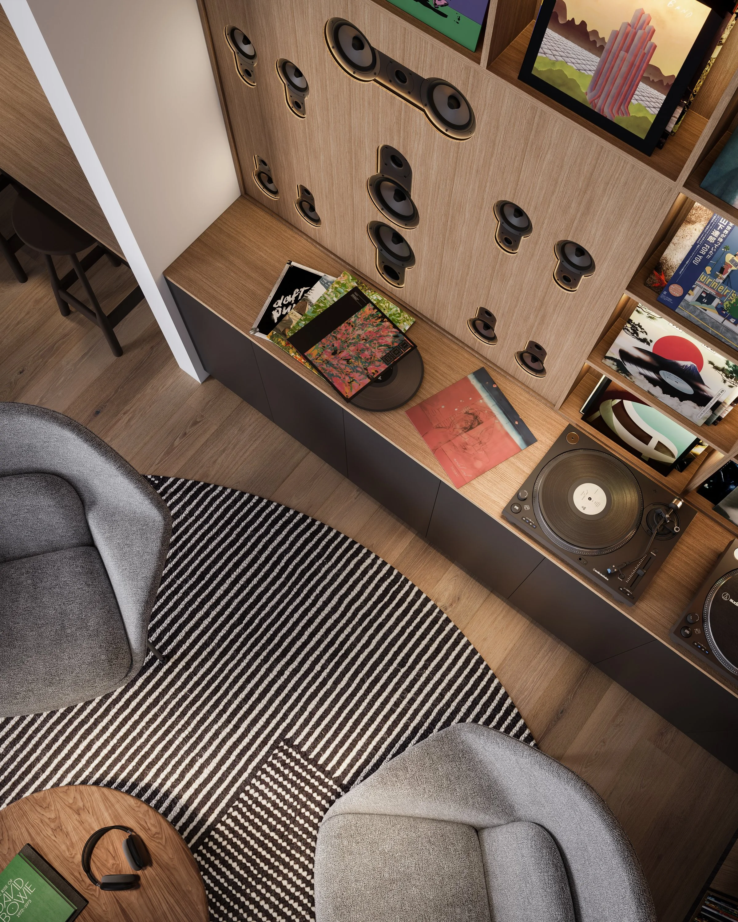 A record player with vinyl records, a wall-mounted speaker system, books, and movies on shelves, with a gray armchair and a black-and-white striped rug in a modern living room.