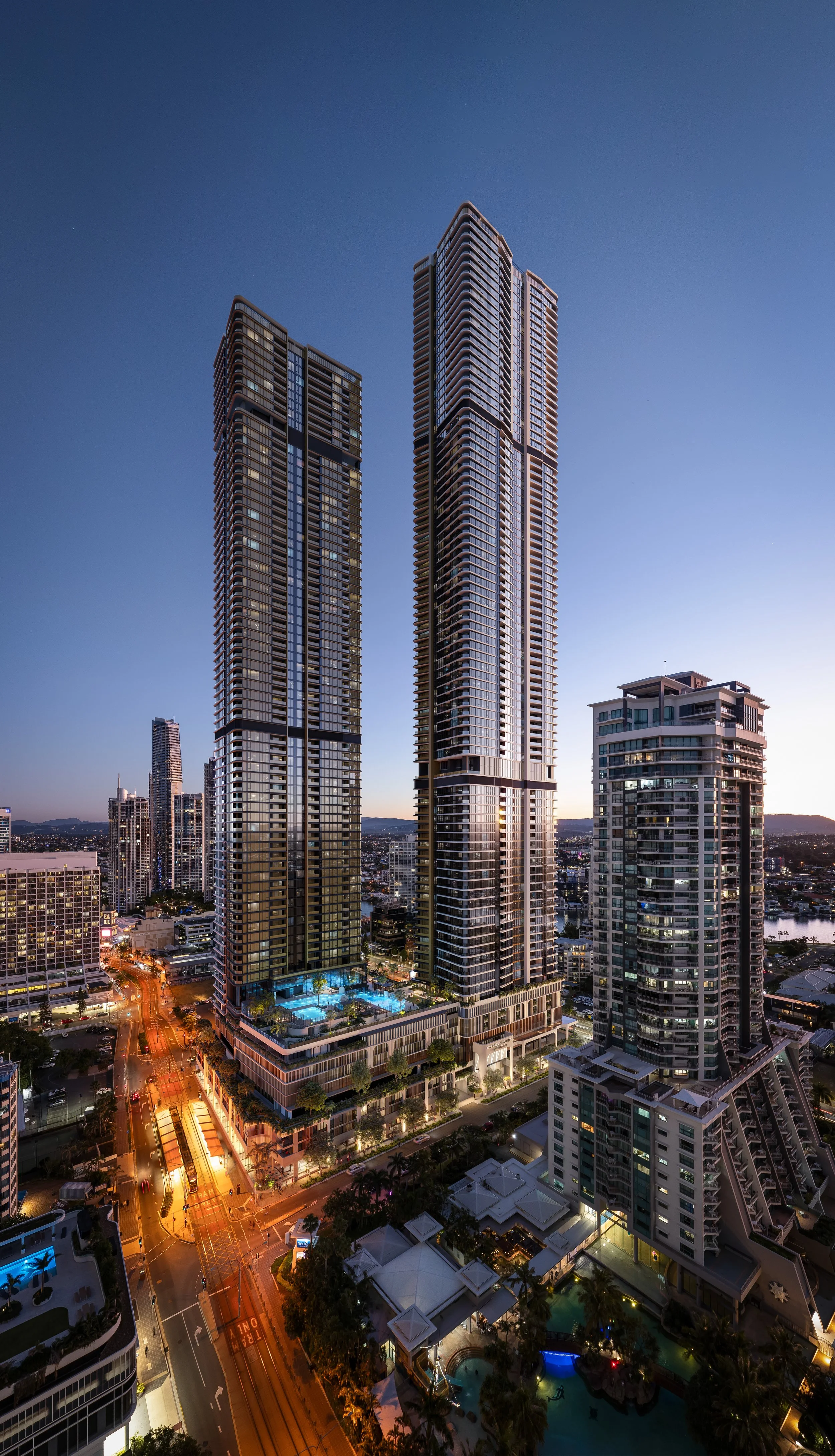 Nighttime cityscape with three modern skyscrapers and surrounding buildings, illuminated streets, and a swimming pool.
