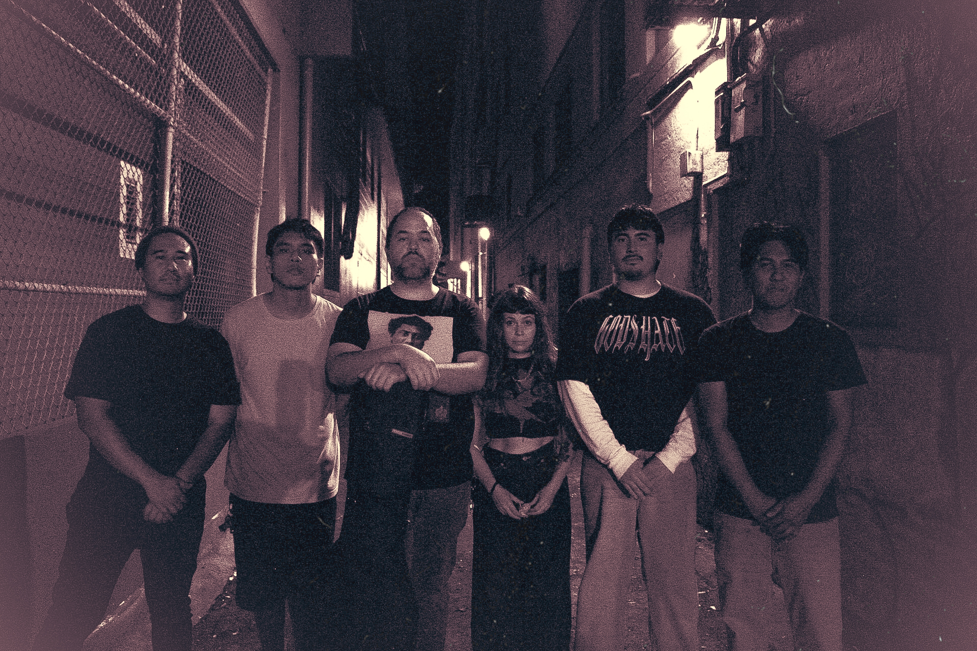 Six people standing in an urban alleyway at night with dim lighting.