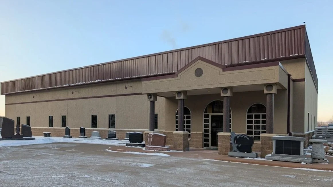 La Crosse Memorials in La Crosse Wisconsin. A business with a beige exterior, brown roof, and several gravestones in front, indicating it is a funeral home or cemetery.