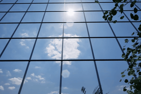 Reflective commercial glass windows showing sunlight and clouds.