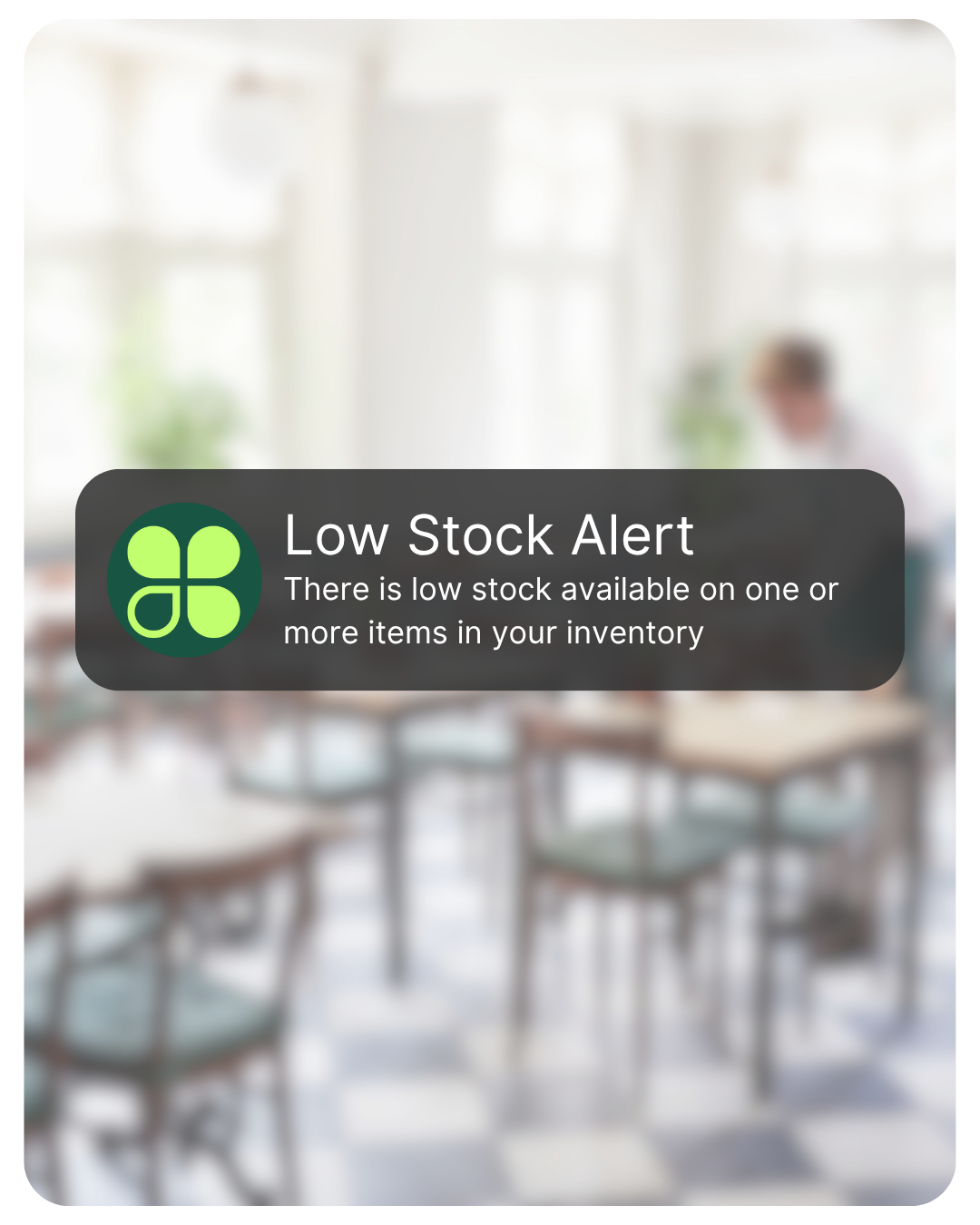A blurred image of a bright room with tables and chairs and a person working at a desk, overlaid with a low stock alert message.