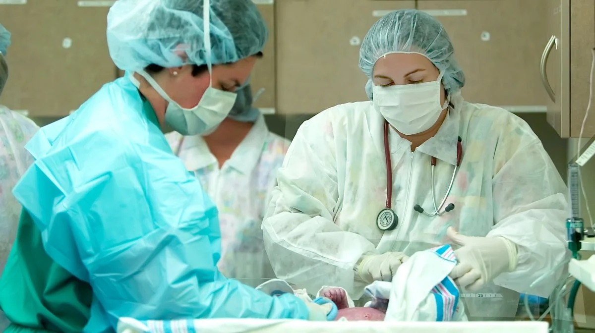 Medical team in surgical gowns, masks, and gloves performing a procedure on a patient, possibly an animal, in a clinical setting.