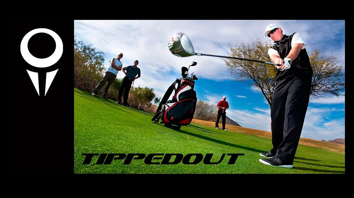 A golfer taking a swing on the golf course with three spectators watching, and a golf bag in the grass nearby, under a partly cloudy sky.