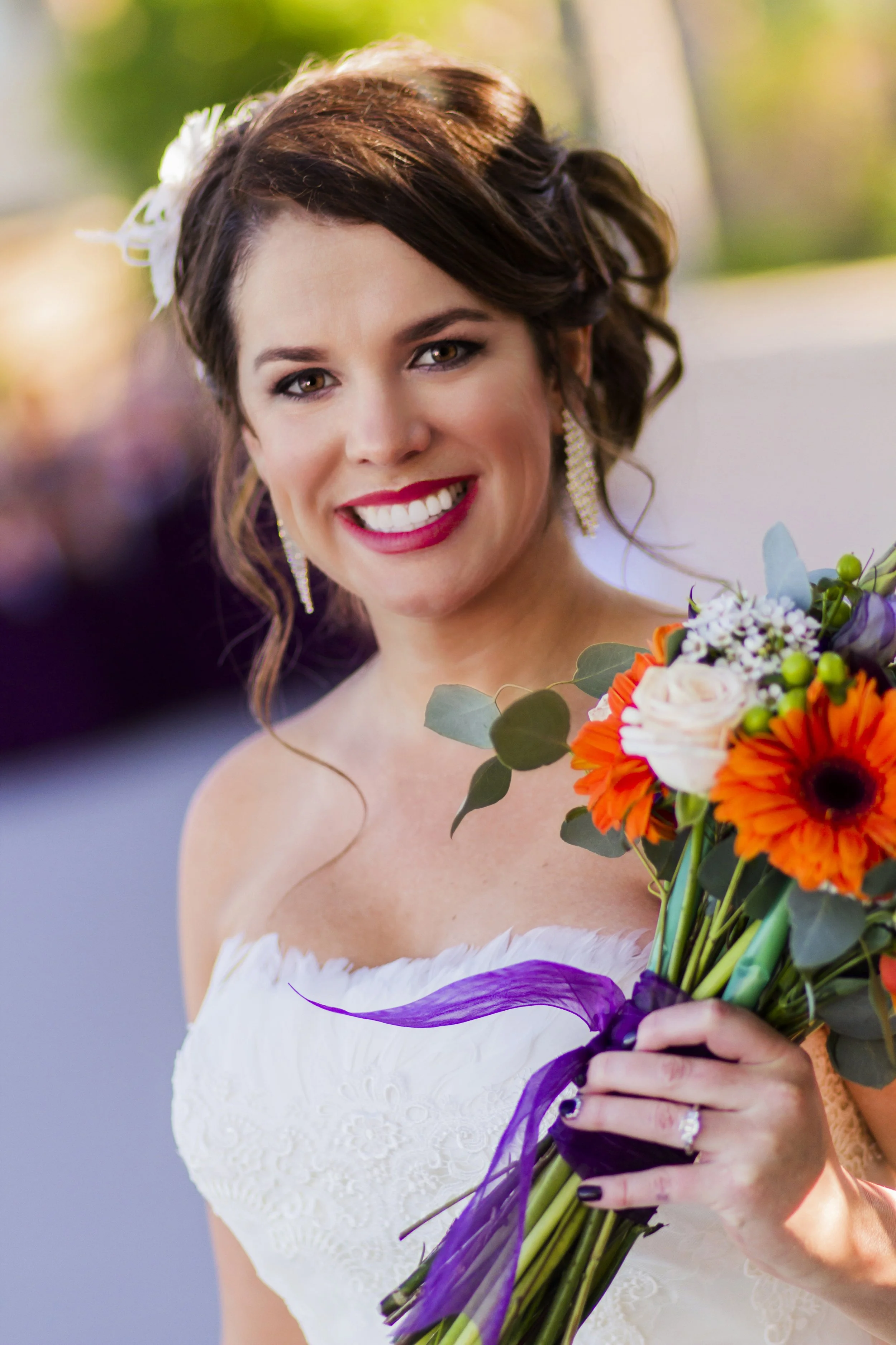 A smiling woman in a white dress holding a colorful bouquet of flowers, with an outdoor blurred background.