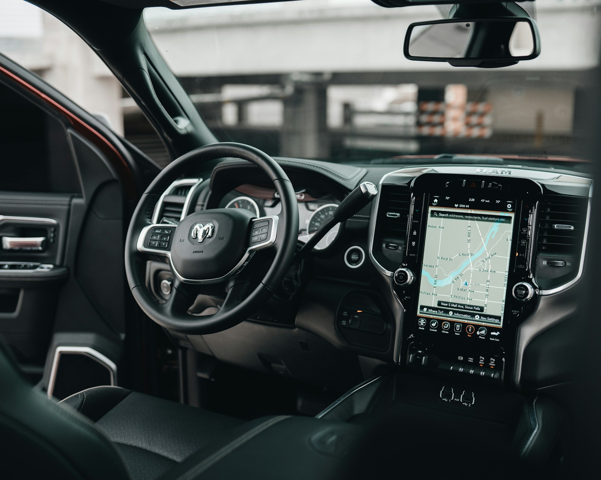 View of the interior of a pickup truck, showing the steering wheel with a Dodge logo, a digital display screen with a GPS map, and various dashboard controls.