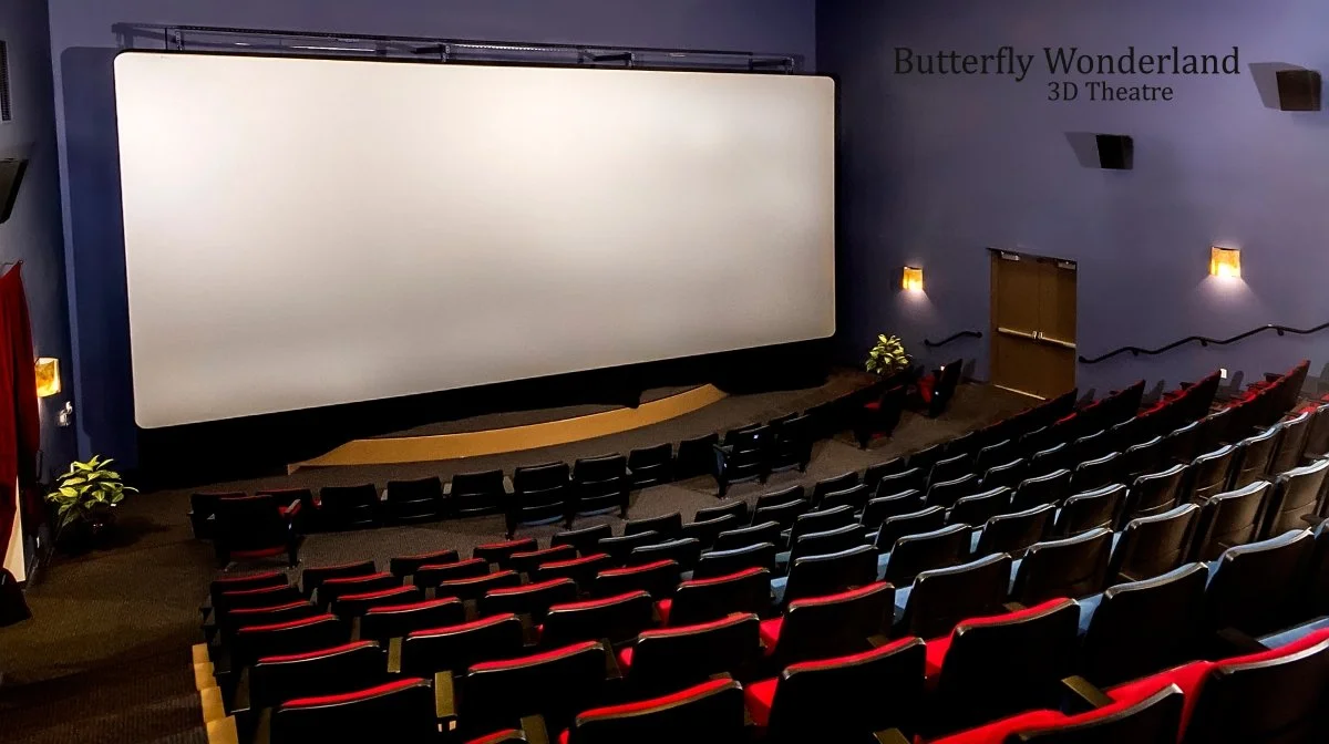 Interior of a movie theater showing 'Butterfly Wonderland 3D Theatre' with empty red and black seats facing a large blank projection screen.