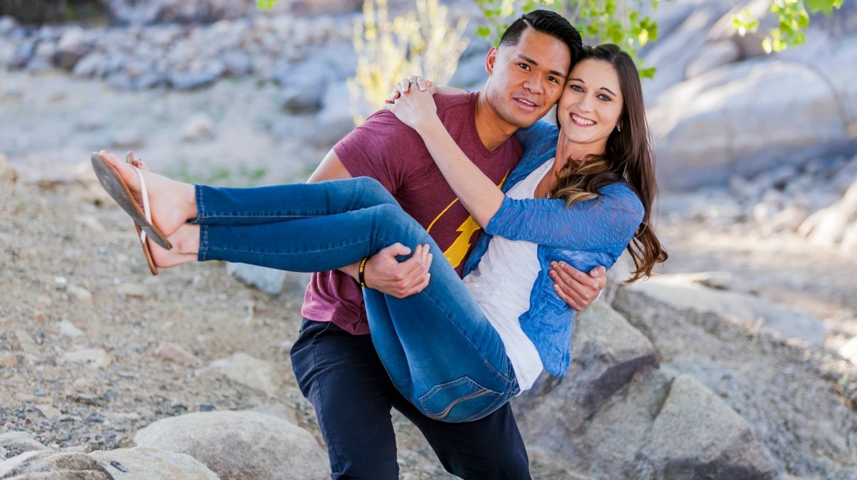 A happy couple outdoors, with the man holding the woman in his arms, both smiling.