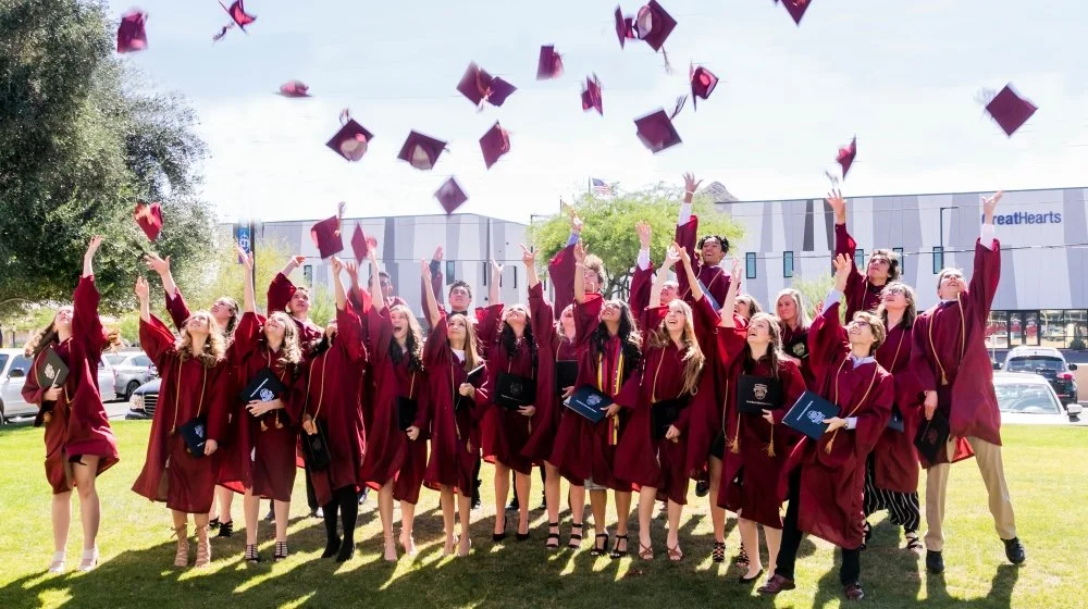 Graduates in maroon caps and gowns celebrating outdoors, throwing their caps in the air.