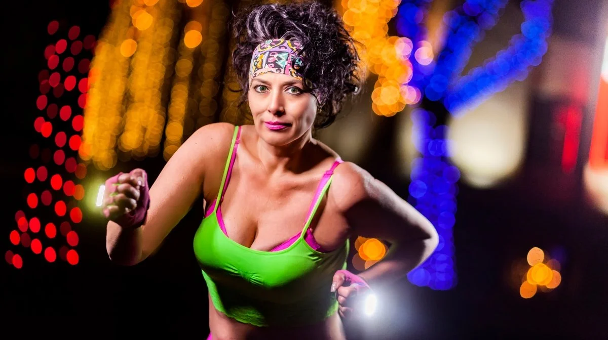 A woman in a green tank top and colorful headband running at night with colorful blurred lights in the background.